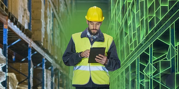 Man in high visibility vest and hard hat walking through warehouse holding an iPad using ClassIT+
